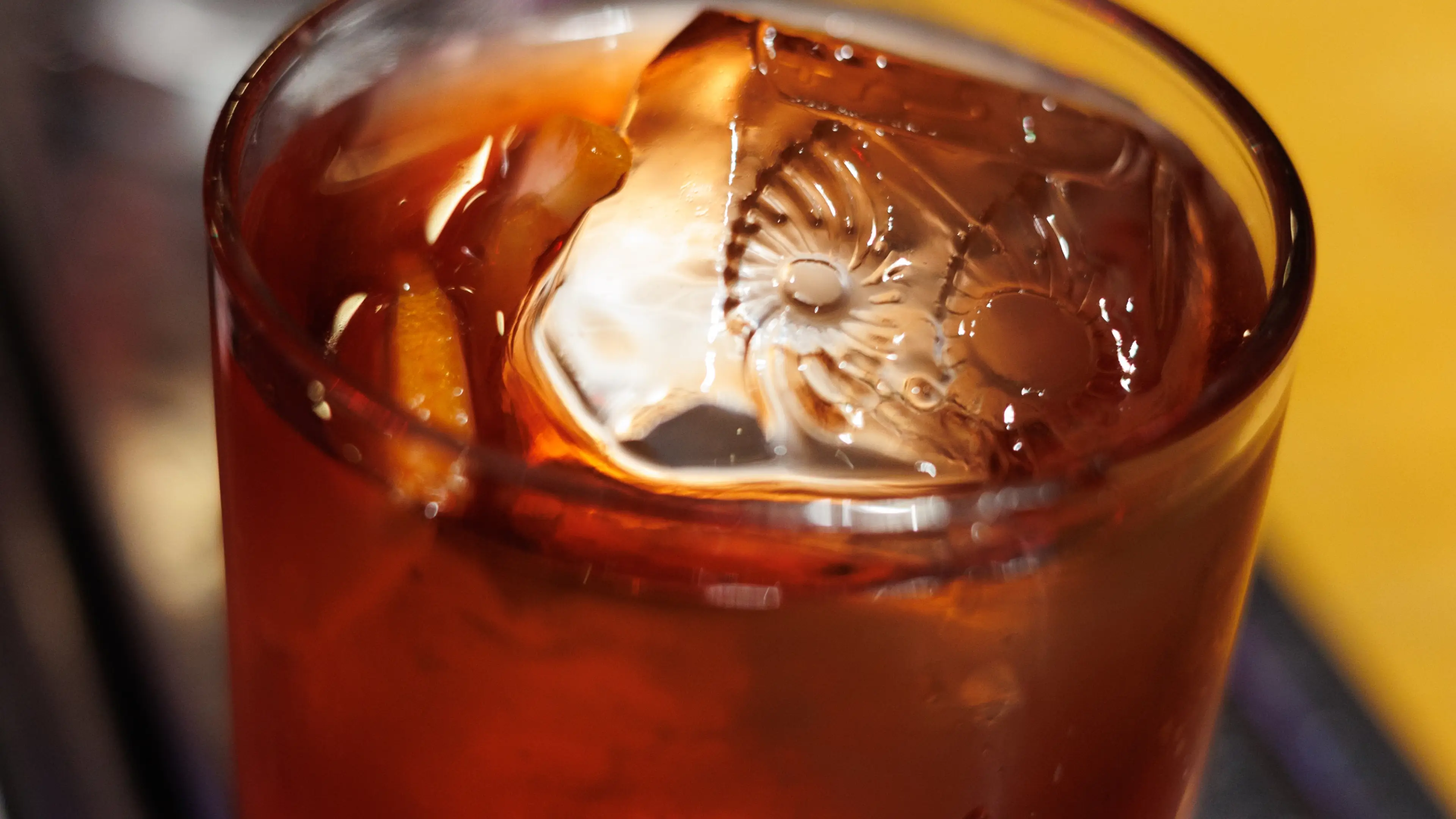 Foto bem próxima e detalhada de um drink do OIDĒ em copo de vidro. Na superfície um cubo de gelo com a gravação do símbolo do OIDĒ.