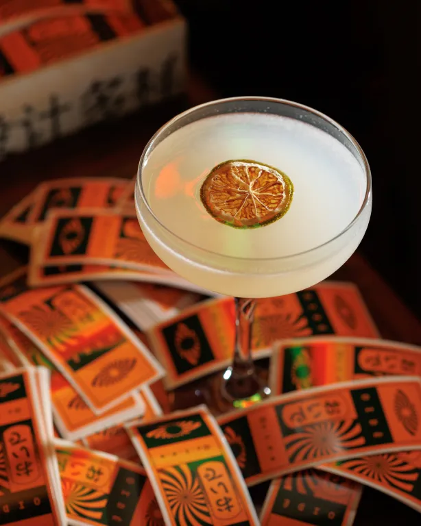 Foto de drink do OIDĒ em taça de vidro com uma rodela limão no topo.